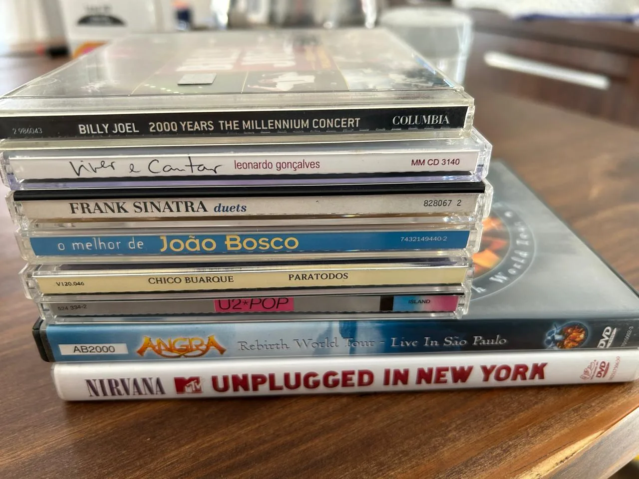 Pilha de seis CDs e dois DVDs comprados em um sebo, com Billy Joel no topo.
