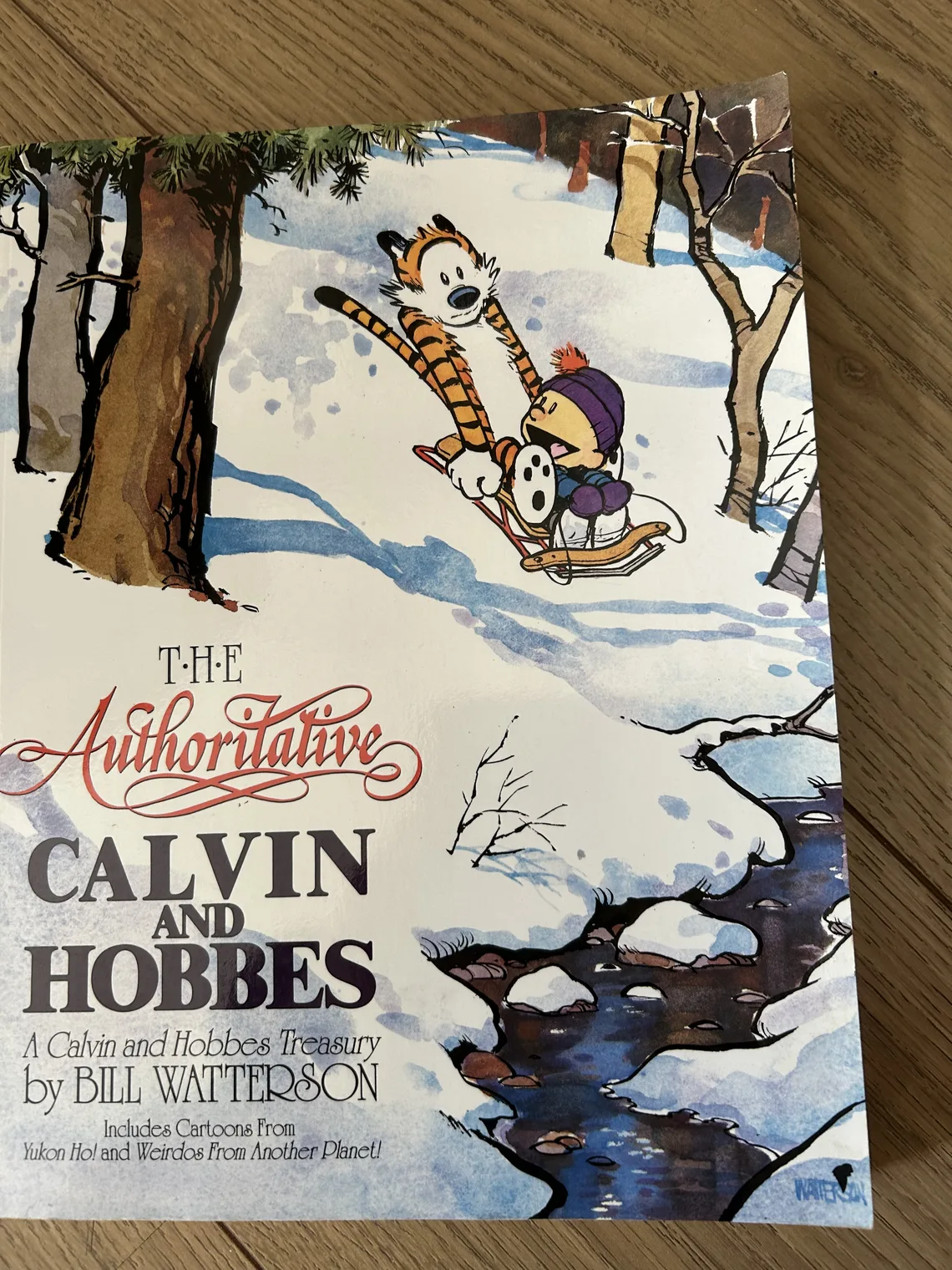 Capa do livro The Authoritative Calvin and Hobbes, fotografada sobre uma mesa de madeira.