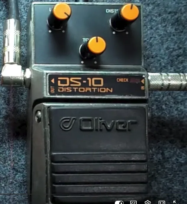 Pedal Oliver DS-10 Distortion preto com três controles laranja, conectado por cabos.