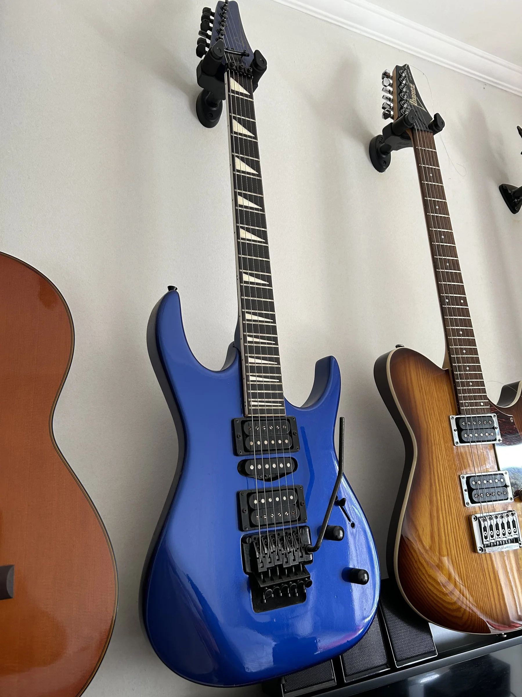 Guitarra elétrica azul pendurada na parede, entre outras guitarras; modelo Golden GH 66.